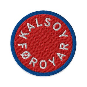 Op de afbeelding: Geborduurde ronde patch met een rode kern en een blauwe rand. De witte tekst "KALSOY FØROYAR" is in een cirkel geborduurd. Deze patch is bedoeld voor kleding of accessoires.