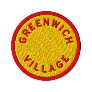 Könnte beinhalten: Ein kreisförmiger gestickter Aufnäher mit einer leuchtend gelben Mitte und dem roten Text GREENWICH VILLAGE, der oben und unten gebogen ist. Der Aufnäher ist mit einem dicken, durchgehend roten Stickrand um den gesamten Außenumfang versehen.