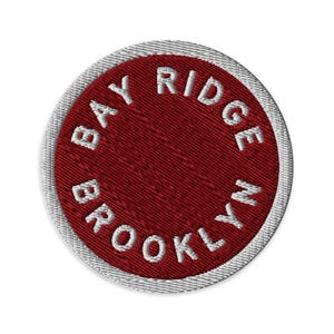 May include: A circular embroidered patch featuring a deep red background with a white border. The text BAY RIDGE BROOKLYN NY is stitched in white capital letters following the circular edge of the patch, creating a clean and bold design.