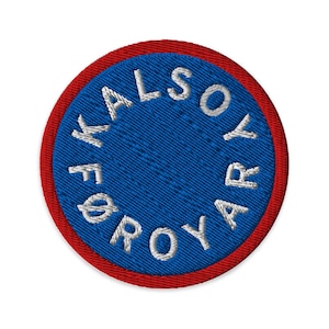 May include: Circular embroidered patch with a blue centre and red border. The white text "KALSOY FØROYAR" is stitched around the blue circle. The patch has a textured appearance.