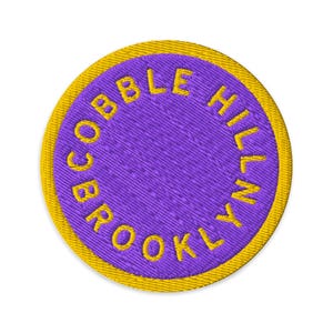 Peut inclure: Écusson brodé circulaire avec le texte "COBBLE HILL BROOKLYN" en jaune sur fond violet. Le patch a une bordure jaune et est destiné aux vêtements ou accessoires.