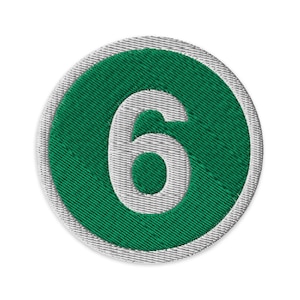 May include: Circular embroidered patch with the number 6 in white, set against a green background. The green circle is framed by a light grey border. The patch has a textured, stitched appearance.