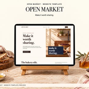 May include: A digital tablet displaying the Open Market website template on a wooden stand. The screen shows a bakery-themed layout with the text "Make it worth sharing" and "The bakery edit" in a clean, serif font against a light background.