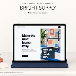 May include: A tablet in a dark blue case displaying the Bright Supply website template. The screen shows the text "Make the next launch easy" and a preview of a laptop on a blue desk. A coral binder clip and a white card sit to the left of the tablet.