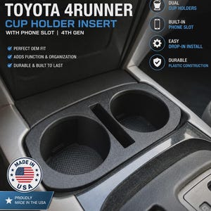 May include: A black plastic cup holder insert for 2003-2009 Toyota 4Runner vehicles. The insert features two circular cup holders and a central rectangular phone slot. Text on the image includes 2003-2009 TOYOTA 4RUNNER CUP HOLDER INSERT.