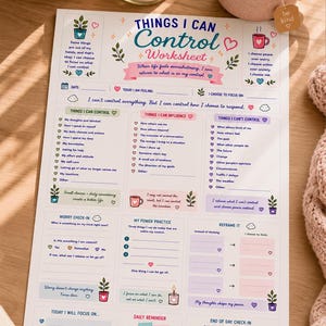 May include: A self-help worksheet titled "Things I Can Control" with a pink and teal design, a candle, a cup of tea, a small potted plant, a notebook, and a pen on a wooden surface. The worksheet has sections for reflection.