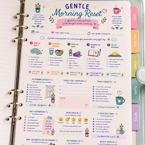 May include: A light blue ring-bound planner open to a page titled Gentle Morning Reset, featuring sections for daily intentions, checklists, affirmations, and mood tracking with colorful icons, text, and tabs for mind, wellness, goals, plans, and notes.