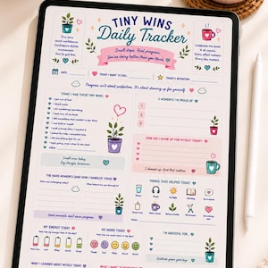 May include: A digital tablet displaying a Tiny Wins Daily Tracker template with sections for tracking mood, energy, gratitude, and daily accomplishments. The interface features pastel colors, floral illustrations, and motivational text like Choose Peace on a mug.