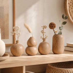 Peut inclure: Un ensemble de quatre vases en bois clair avec des motifs de grain visibles, chacun contenant une tige botanique séchée. Les vases varient en forme, incluant des modèles sphériques, en forme de gourde et cylindriques, alignés sur une surface.