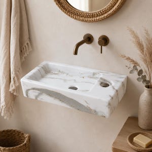 Peut inclure: Un lavabo rectangulaire mural en marbre blanc avec des veines grises marquées. Le lavabo présente un trou d'évacuation et un orifice latéral pour la robinetterie, accompagné d'un robinet mural en bronze et d'une poignée cylindrique.