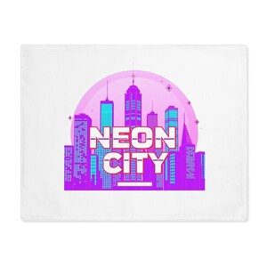 Op de afbeelding: Witte kussensloop met een neon stadsontwerp. Het ontwerp omvat een stadsgezicht met paarse, blauwe en roze gebouwen, een roze cirkelvormige achtergrond en de woorden "NEON CITY" in witte letters.