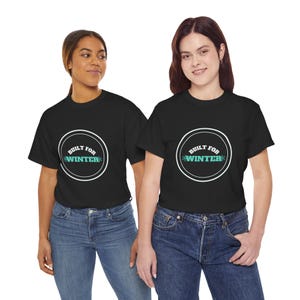 Op de afbeelding: Een zwart t-shirt met korte mouwen en een witte cirkelvormige afbeelding op de borst. Binnenin de cirkel staat de tekst BUILT FOR WINTER in witte en turquoise letters, geaccentueerd met kleine sneeuwvlokpictogrammen naast het woord WINTER.