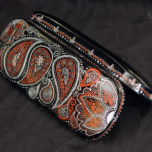 Case for glasses, hand-painted with red and silver paisley design. The case is open, on the black velvet material to show the contrast.
