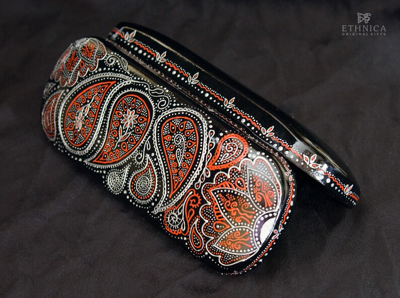Case for glasses, hand-painted with red and silver paisley design. The case is open, on the black velvet material to show the contrast.