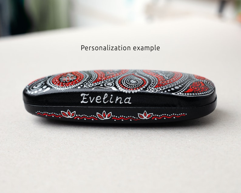 Eyeglasses case, hand-painted with red and silver paisley design. Example of personalization with the name painted on the front of the case. Close-up view from the side.