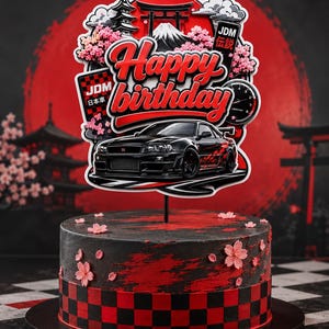 Pode incluir: Um topo de bolo com um carro esportivo preto, o texto Happy Birthday, um sol vermelho, um torii, um pagode e flores de cerejeira. O bolo abaixo é preto e vermelho com um padrão xadrez e detalhes de flores de cerejeira rosas nas laterais.