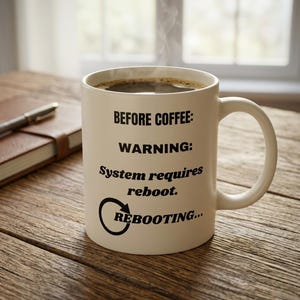 May include: A white ceramic mug filled with dark coffee, featuring black printed text that reads: BEFORE COFFEE: WARNING: System requires reboot. REBOOTING... with a circular arrow icon. The mug has a standard handle and a smooth finish.
