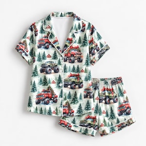May include: A short-sleeve button-down pajama shirt and matching shorts set featuring a repeating pattern of red and green monster trucks carrying Christmas trees, interspersed with evergreen trees and small red houses on a white background.