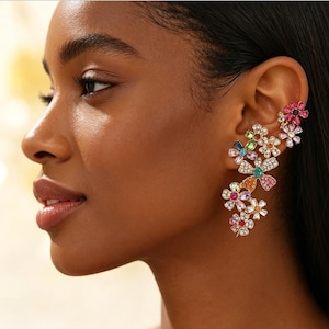 Pode incluir: Uma ear cuff floral com uma cascata de flores coloridas e com joias. As flores são adornadas com várias pedras preciosas coloridas, incluindo rosa, azul, verde e laranja, sobre um metal dourado.