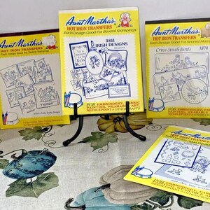 May include: Five different packages of iron-on transfer designs for embroidery, painting, and crafts. Each package features a different design theme, including Irish designs, cross stitch birds, and a variety of other designs. The packages are all yellow with blue and white text.
