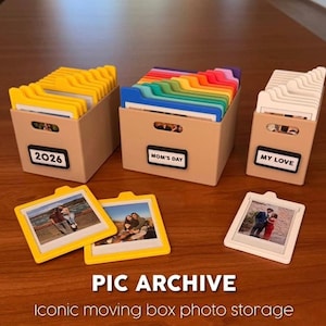 以下が含まれることがあります： ベージュ色の写真収納ボックス。カラフルなタブとフォトフレーム付き。ボックスには「2026」、「Mom's Day」、「My Love」とラベルが貼られています。フォトフレームは黄色と白です。「PIC ARCHIVE」と「Iconic moving box photo storage」の文字が見えます。