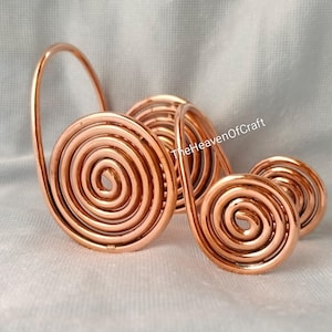 Può includere: Un supporto in filo di rame caratterizzato da molteplici forme a spirale interconnesse di varie dimensioni. La struttura metallica presenta una calda tonalità bruno-rossastra con finitura lucida. Il testo TheHeavenOfCraft è visibile.