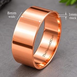 Könnte beinhalten: Ein polierter kupferfarbener Ring mit einer glatten, flachen Oberfläche. Das Band ist 8 mm breit und 1 mm dick, wie durch den sichtbaren Messtext angegeben. Die Innenseite des Rings trägt den eingravierten Text TheHeavenOfCraft in dunkler Schrift.