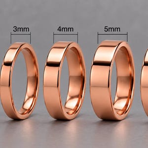 Puede incluir: Cinco anillos pulidos de tono oro rosa dispuestos en fila, cada uno con un ancho de banda diferente. Los anchos están claramente etiquetados sobre cada anillo como 2mm, 3mm, 4mm, 5mm y 6mm, mostrando la progresión de tamaño de menor a mayor.
