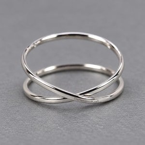 Op de afbeelding: Een gepolijste zilverkleurige ring met een kruisend ontwerp van twee dunne, gladde banden die aan de voorzijde samenkomen. De tekst TheHeavenOfCraft is duidelijk gegraveerd op de onderste band van de ring, die een reflecterende metalen afwerking heeft.