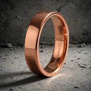 May include: A polished copper-colored ring with a smooth, flat outer surface. The exterior is engraved with the text 5 MM, while the interior band features the engraved text TheHeavenOfCraft. The ring has a simple, circular band design.