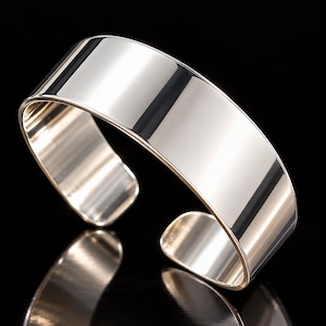 May include: A wide, polished silver-tone cuff bracelet with a smooth, reflective surface. The bracelet features an open-ended design, allowing for easy adjustment. The metal has a high-shine finish that catches the light, creating bright highlights.