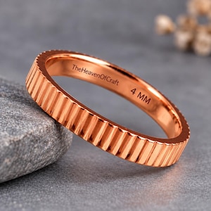 May include: A rose gold-toned ring with a vertical ribbed texture around the outer band. The interior of the ring is engraved with the text TheHeavenOfCraft and 4 MM, indicating a width of 4 millimetres for this metallic band.
