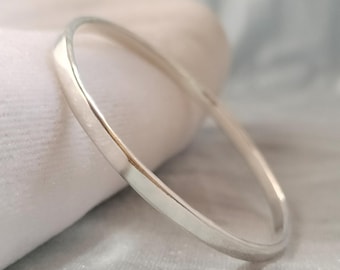 Può includere: Un bracciale rigido in argento lucido con una superficie esterna liscia e arrotondata e una finitura metallica riflettente. La fascia circolare presenta uno spessore costante in tutto il design, mostrando un'estetica pulita e semplice senza decorazioni.