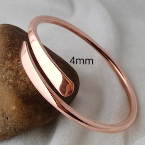May include: A rose gold-colored bypass bangle bracelet with a smooth, polished finish. The metal band features a rounded profile and a width of 4mm as indicated by the text printed on the image. The bracelet has an open design with overlapping ends.
