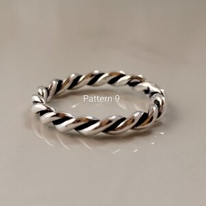 May include: A silver-toned ring featuring a twisted rope design with dark oxidised grooves between the metallic strands. The text Pattern 9 is printed in white in the centre of the ring, which has a polished finish and a continuous circular band.