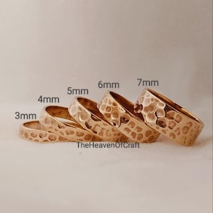 Pode incluir: Cinco anéis dourados com textura martelada, dispostos em fila do menor para o maior. Os anéis estão rotulados com larguras de 3mm, 4mm, 5mm, 6mm e 7mm. O texto TheHeavenOfCraft está impresso na parte inferior da imagem.