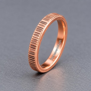 Può includere: Un anello color rame con una superficie esterna testurizzata e a coste con scanalature verticali. La fascia ha una superficie interna liscia e include il testo TheHeavenofCraft stampato in nero sul lato della fascia dell'anello.
