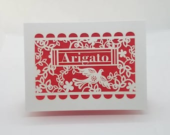 Arigato.  Say Thank you in Japanese in our papel picado design with a dove.  We laser cut the card stock and add colored tissue paper to it.