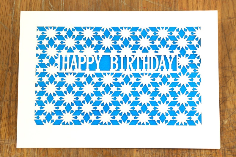 May include: A white card with a blue patterned background. The pattern is made up of stars and diamonds. The words "HAPPY BIRTHDAY" are cut out of the card.