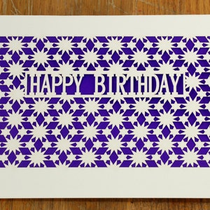 May include: A white card with a purple background and a cut-out design of stars and the words "Happy Birthday".