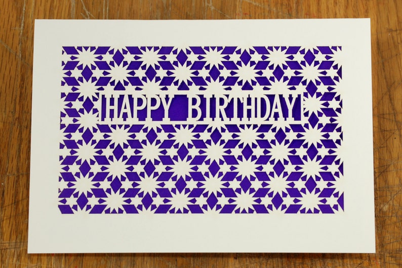 May include: A white card with a purple background and a cut-out design of stars and the words "Happy Birthday".