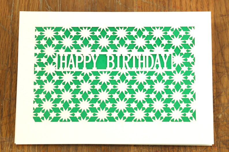 May include: White card with a green geometric pattern cut out to reveal the words "Happy Birthday".