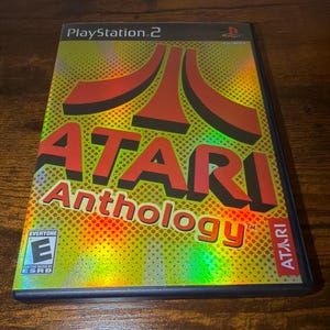 May include: A PlayStation 2 game case for Atari Anthology. The cover features the Atari logo in red, with the title in red and yellow. The background has a holographic effect. The game is rated "Everyone" by the ESRB.