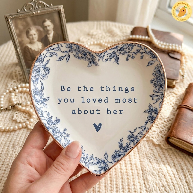 May include: Heart-shaped ceramic dish with a blue floral design and gold trim. The dish features the text "Be the things you loved most about her" and a small blue heart. Decorative item.