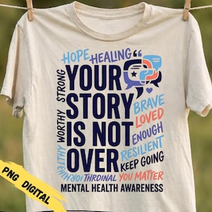 May include: A cream-colored t-shirt featuring dark blue, light blue, and coral text that reads: YOUR STORY IS NOT OVER, HOPE, HEALING, STRONG, WORTHY, BRAVE, LOVED, ENOUGH, RESILIENT, KEEP GOING, YOU MATTER, MENTAL HEALTH AWARENESS, and speech bubbles.