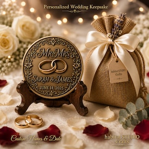 Peut inclure: Un médaillon rond couleur bronze sur un support en bois foncé, gravé avec "MR & MRS", "SARAH & JAMES" et "JUNE 14, 2025". À côté se trouve une pochette en toile de jute avec un ruban en satin crème, un brin de lavande et une étiquette "habitat STUDIO Crafts".