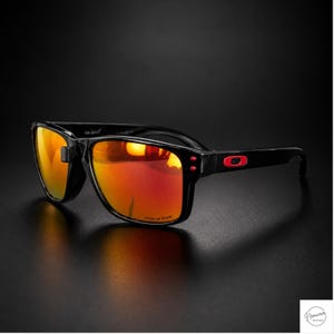 May include: Black sunglasses featuring rectangular frames and reflective orange-red lenses. The temples display a small red rectangular logo emblem near the hinges. The lenses are etched with the word Prizm in the lower corner of the right lens.