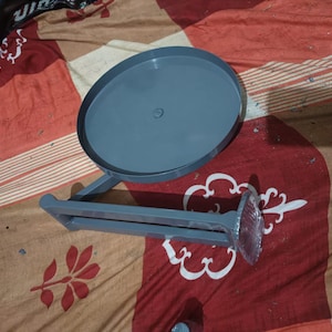 May include: A grey metal wall-mounted organiser featuring a circular tray attached to a horizontal bar with a flat mounting plate at one end. The structure is finished in a solid matte grey colour and includes a small central screw on the tray.