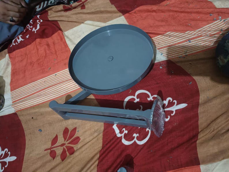 May include: A grey metal wall-mounted organiser featuring a circular tray attached to a horizontal bar with a flat mounting plate at one end. The structure is finished in a solid matte grey colour and includes a small central screw on the tray.