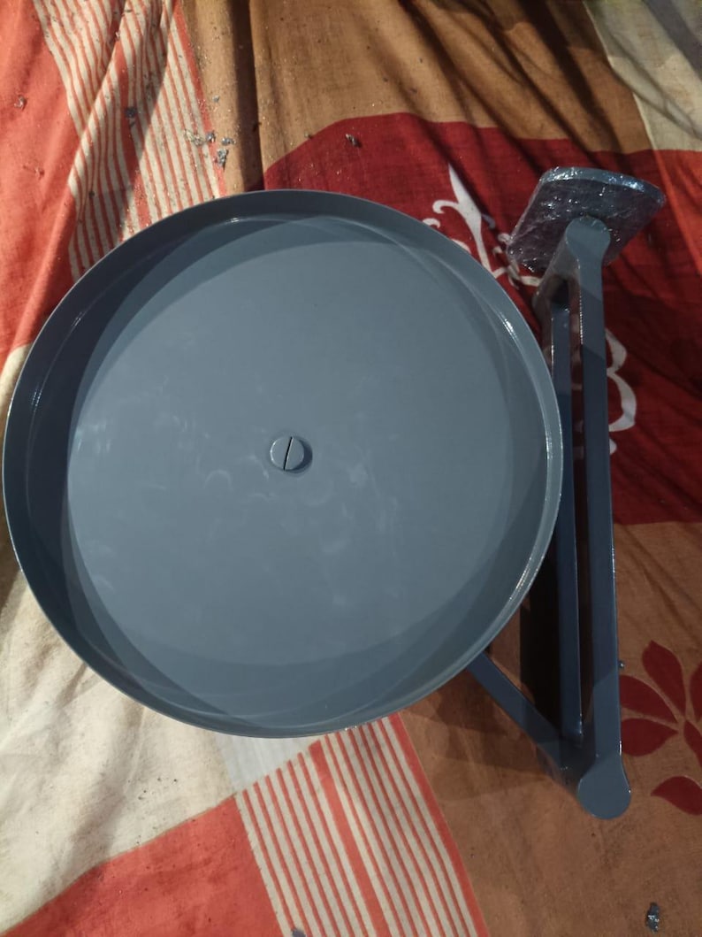 May include: A grey metal circular platform with a central screw, attached to a vertical support arm and a rectangular base plate. The structure features a smooth, uniform grey finish throughout, with a flat, round top surface and a sturdy, angular frame.